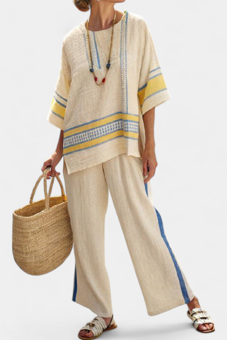 Woman wearing a beige outfit with yellow and blue accents, holding a woven bag on a white background