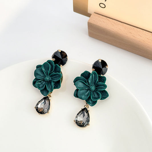 Green floral earrings with black gemstones on a white surface