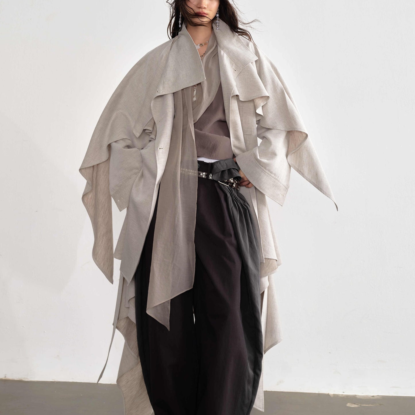 Person wearing a light gray draped coat over a neutral outfit on a white background