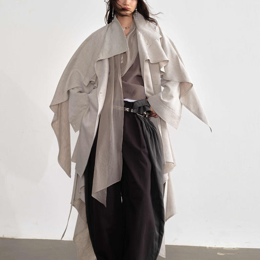 Person wearing a light gray draped coat over a neutral outfit on a white background