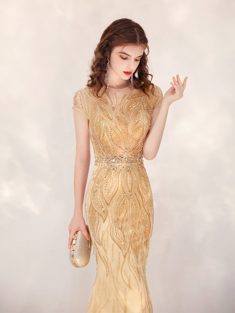 Woman wearing a gold evening gown with intricate detailing on a light background