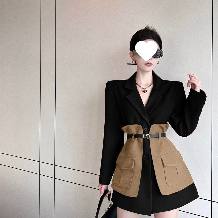 Person wearing a black and brown coat with a belt, standing against a neutral wall.