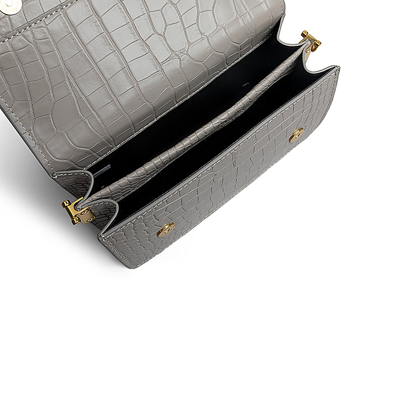 Gray crocodile-patterned handbag with gold hardware on a white background