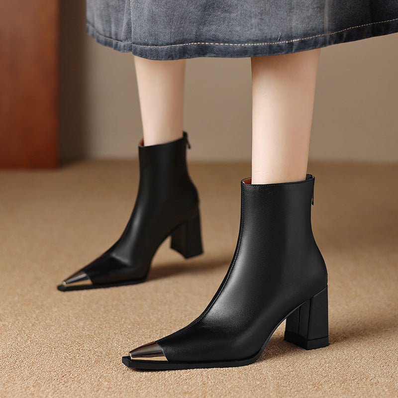 Black pointed-toe ankle boots with block heels and metallic gold toe caps, shown on a model wearing a denim skirt.