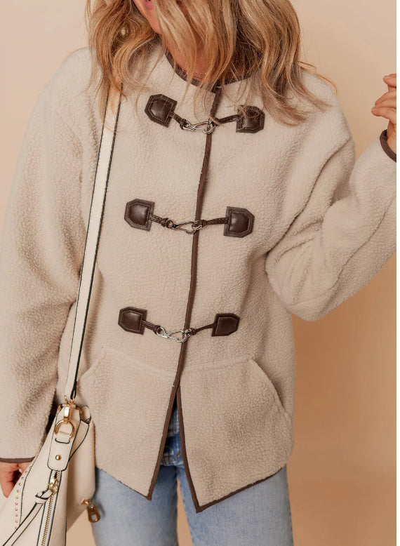 Person wearing a beige duffle coat with brown buttons on a beige background