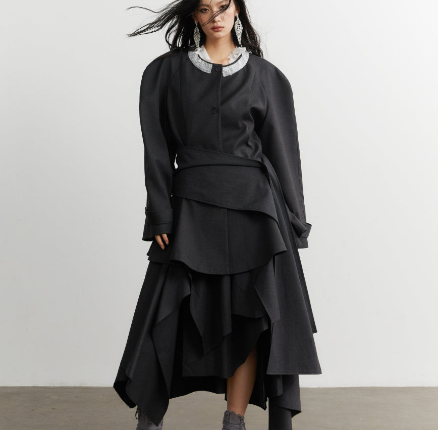 Woman wearing a black layered outfit with a white collar against a plain background