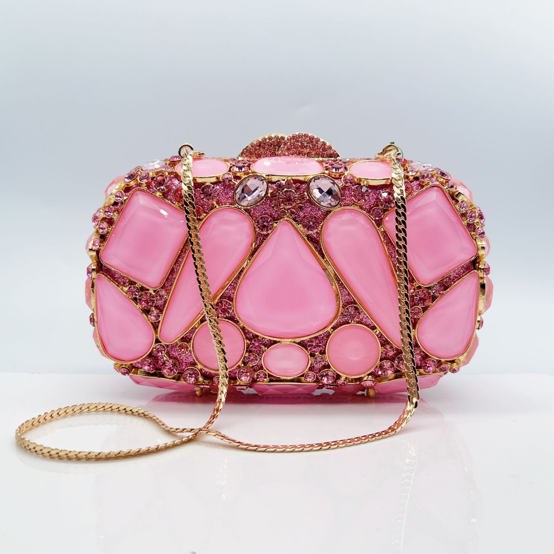 Pink clutch bag with gemstone embellishments on a light gray background