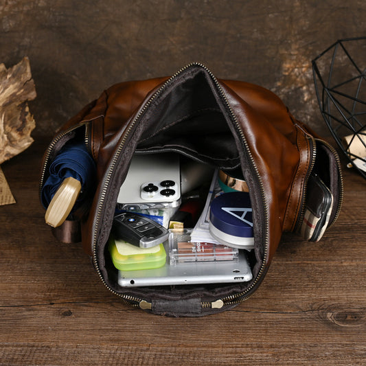 Open brown leather bag with various items on a wooden surface