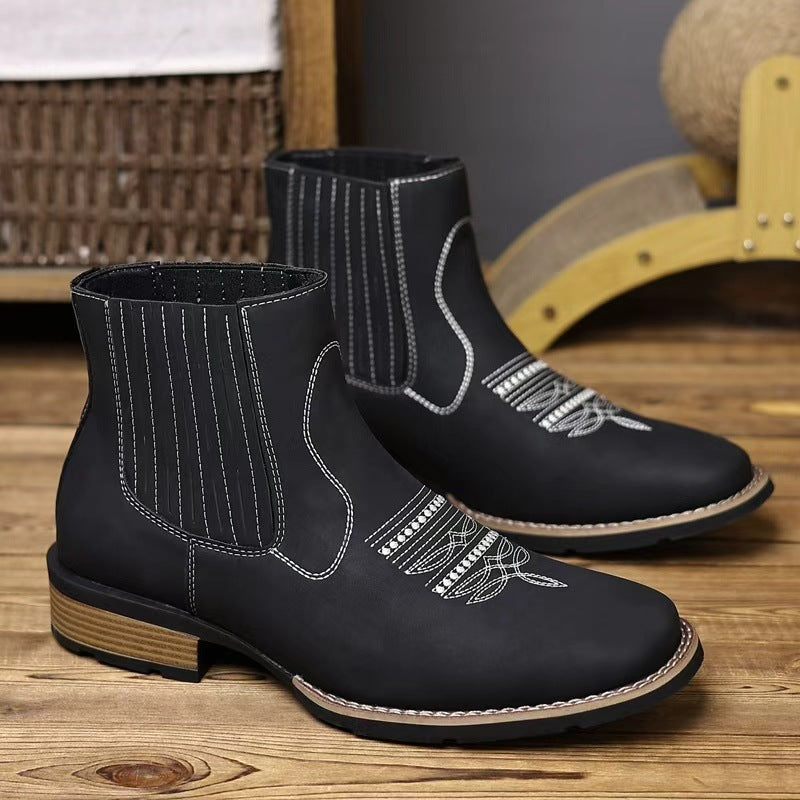 Black leather boots with white stitching on a wooden floor