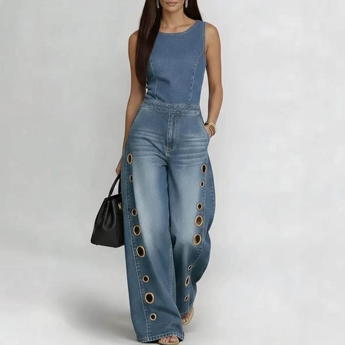 Woman wearing a blue denim jumpsuit with grommet details on a white background