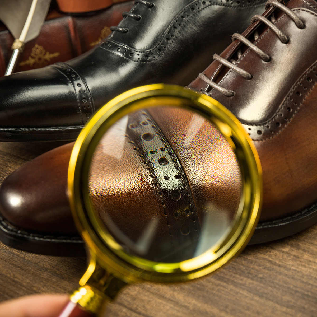 Brown leather shoes with a magnifying glass inspecting the texture on a wooden surface