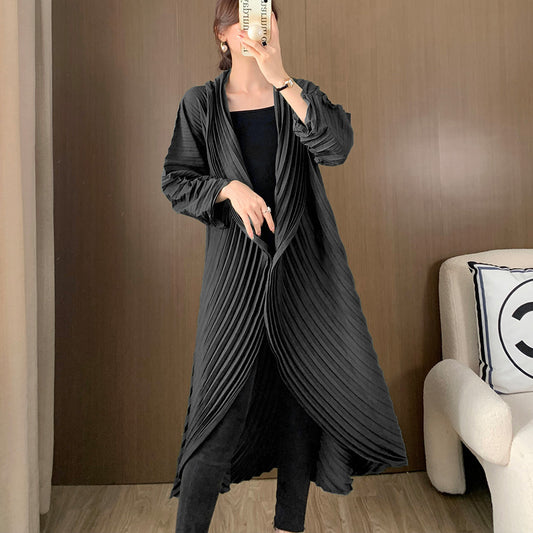 Person wearing a long, dark gray pleated dress against a brown wall.