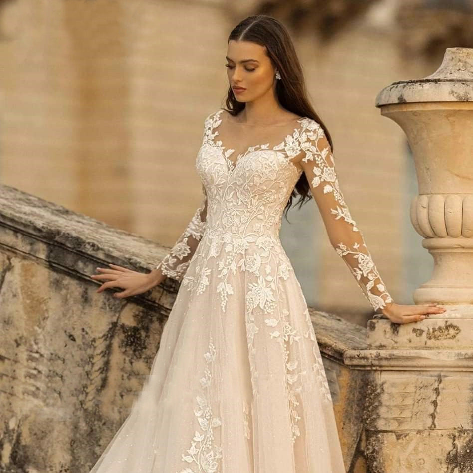 Woman in a lace wedding dress standing against an old stone wall.