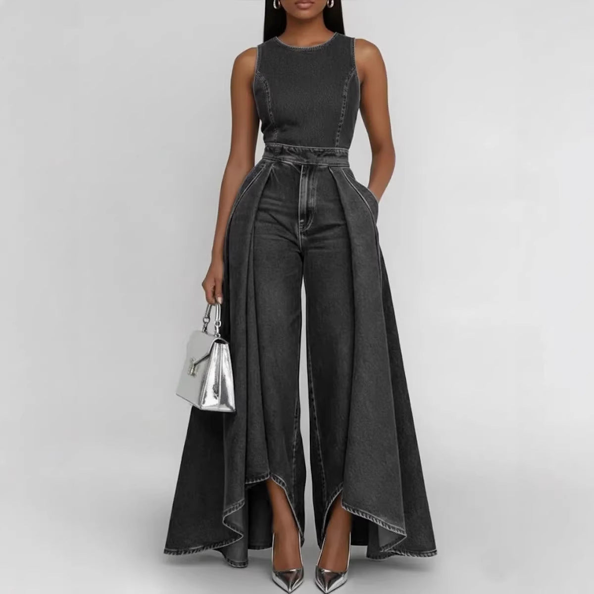 Woman wearing a black denim jumpsuit with a silver handbag on a light gray background