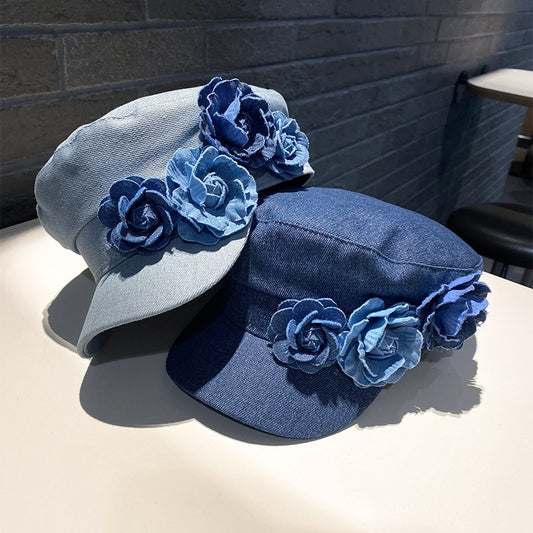 Two denim hats with floral embellishments on a table against a brick wall.