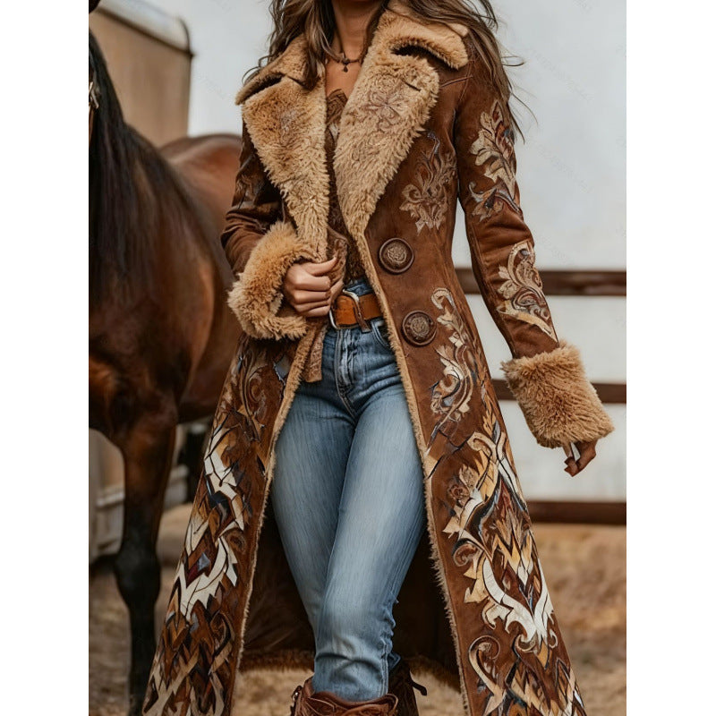A woman wearing a long brown suede-like coat with beige faux-fur trim and ornate western-style embroidery, paired with blue jeans and brown boots, standing in front of a horse in a rustic indoor setting.