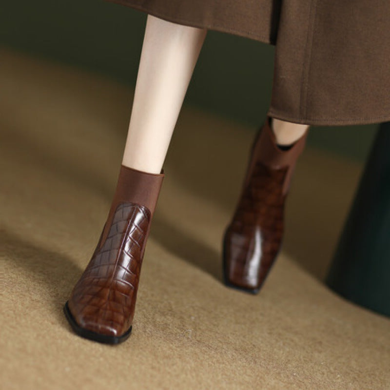 Brown leather boots worn with a brown skirt on a beige surface
