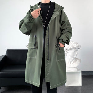 Person wearing a green raincoat in an indoor setting with a black couch and white sculpture.