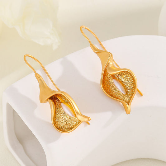 Gold leaf-shaped earrings on a white surface with a light background