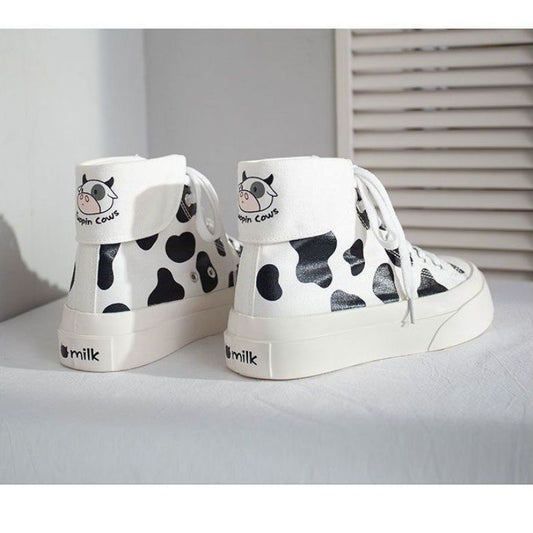 White high-top sneakers with black cow print and 'milk' text on a light gray surface.