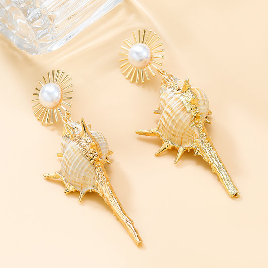 Gold and shell earrings with pearl accents on a beige background
