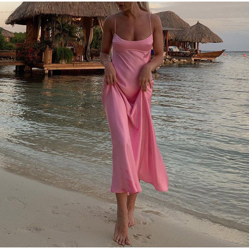 Woman in a pink dress standing on a beach with huts and water in the background by millivan