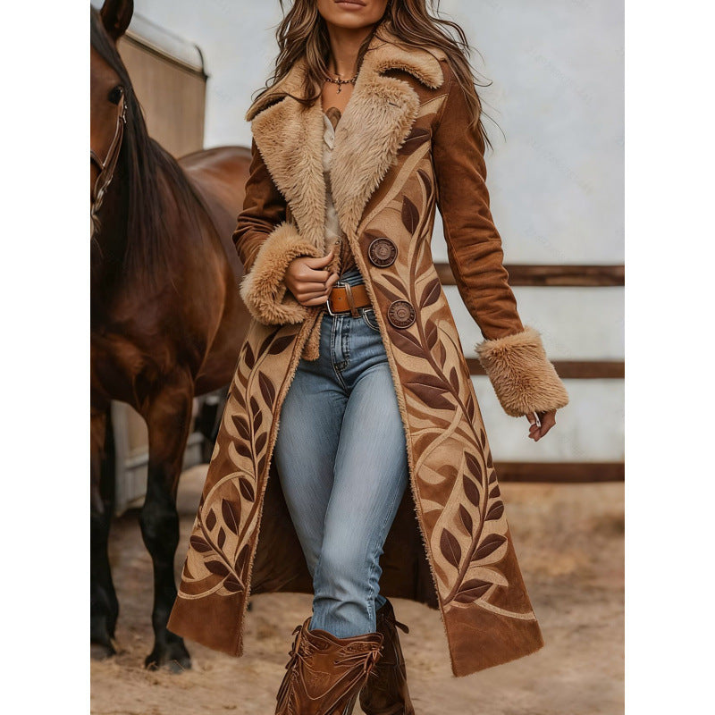 A woman wearing a long brown suede-like coat with a large beige faux-fur collar and leaf embroidery, standing in a barn next to a horse.