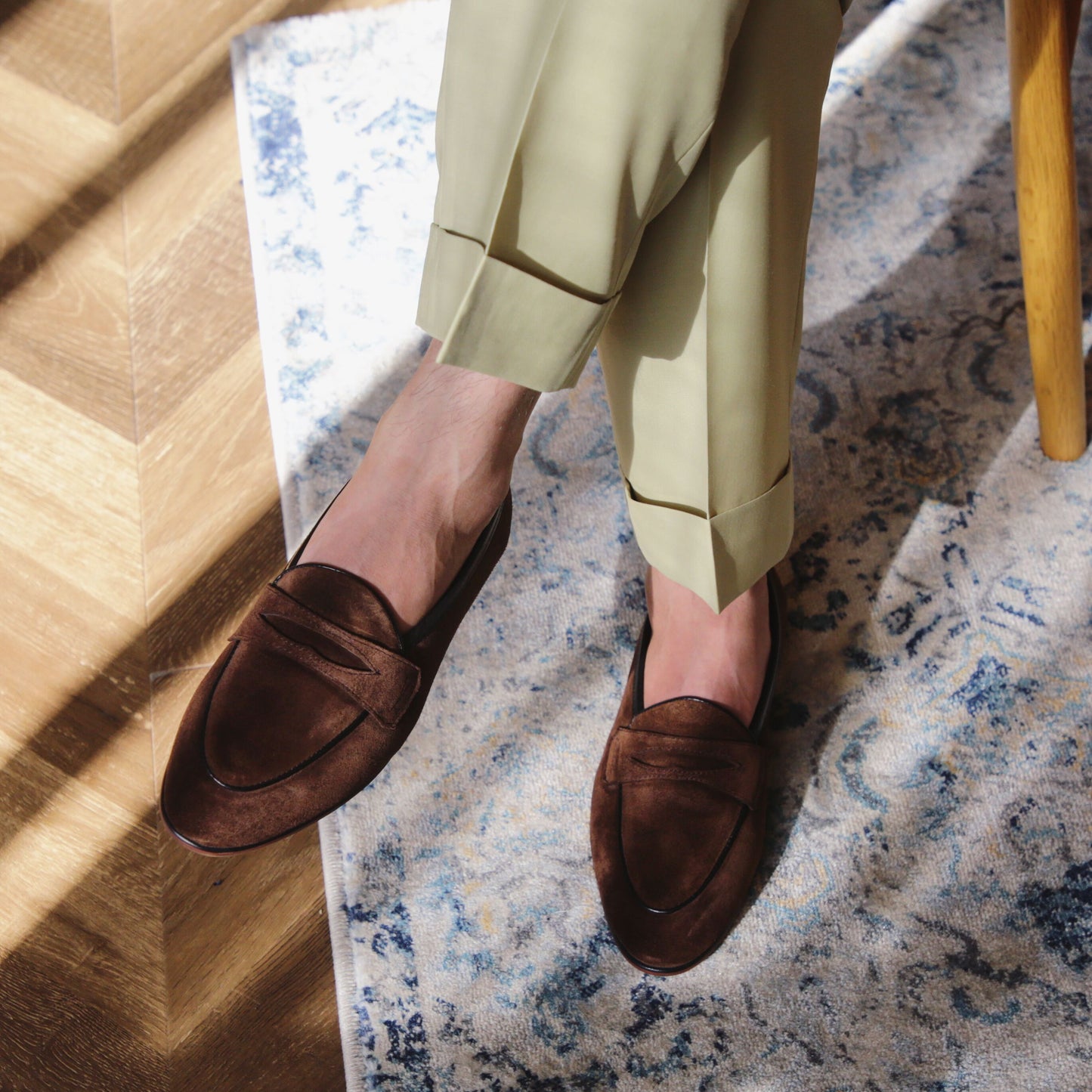 Brown loafers worn with light green pants on a patterned rug.