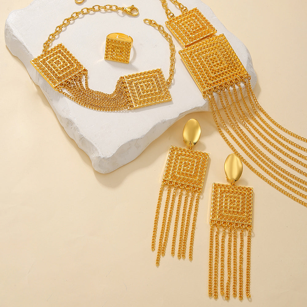 Gold jewelry set including necklace, earrings, and bracelet on a textured white surface.