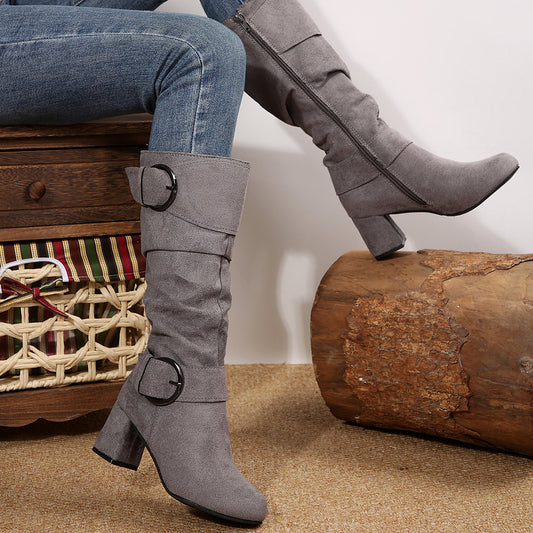 Gray knee-high boots with buckle details worn by a person sitting on a wooden log.