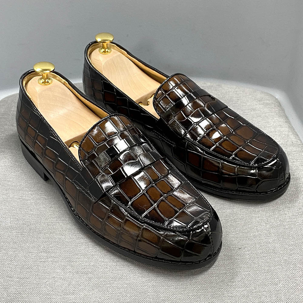 Pair of black crocodile-patterned loafers on a light gray surface.