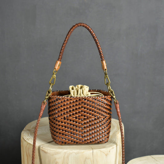 Woven handbag with leather handle and strap on a wooden stool against a gray background