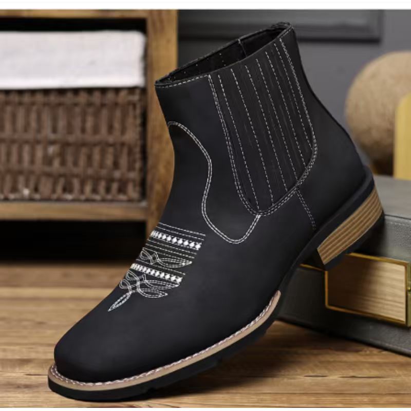 Black ankle boot with decorative stitching on a wooden surface
