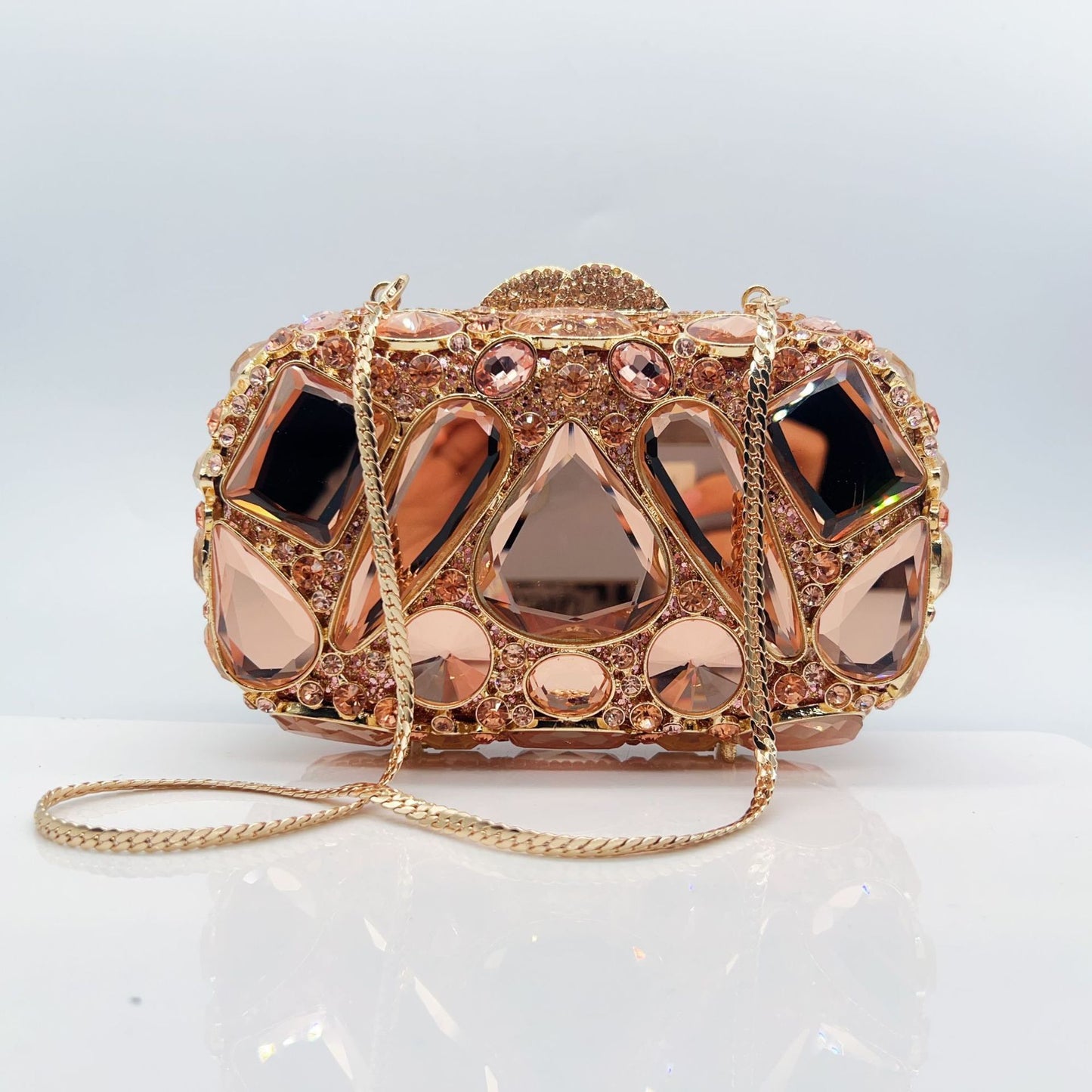 Rose gold clutch bag with gemstone-like embellishments on a white background