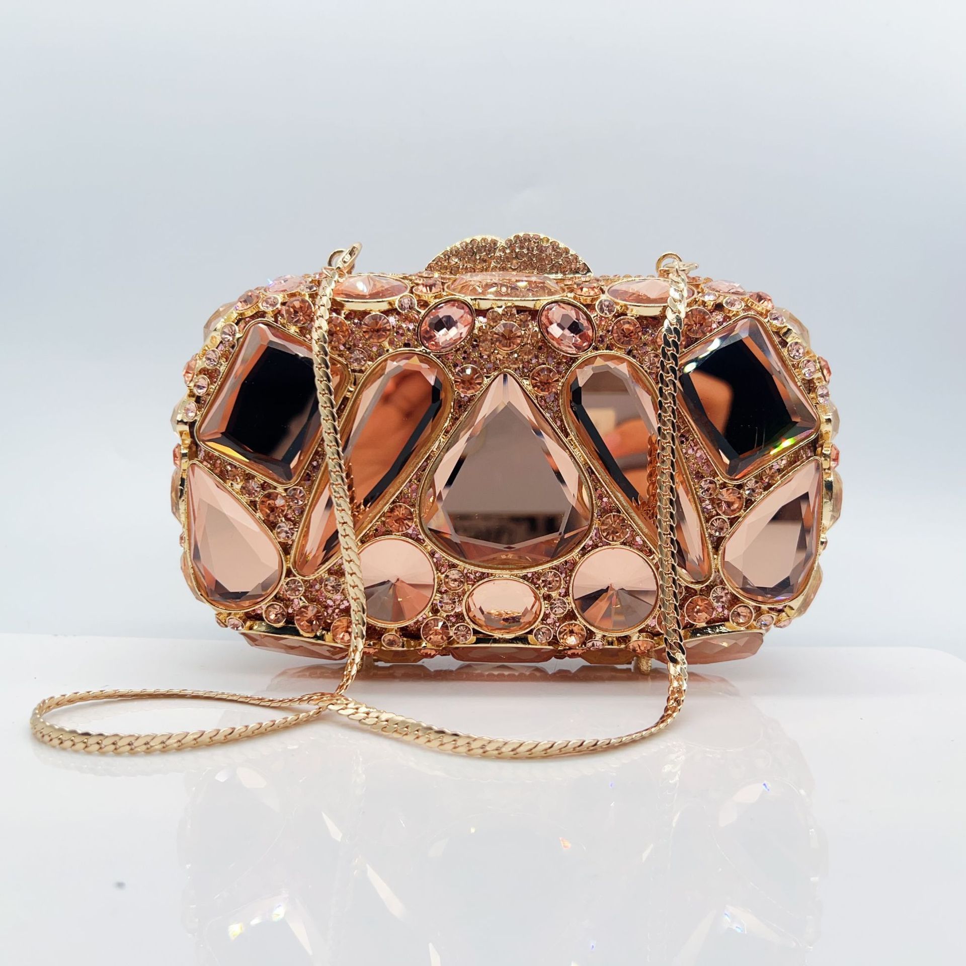 Rose gold clutch bag with gemstone-like embellishments on a white background