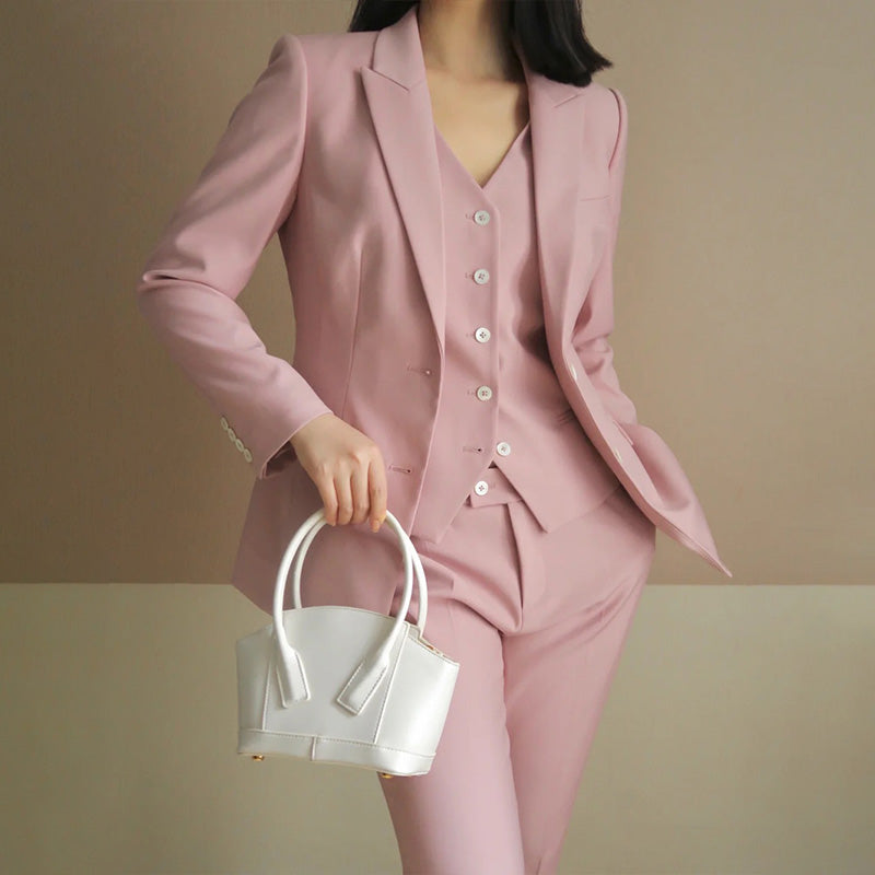 Person wearing a pink suit holding a white handbag against a beige background