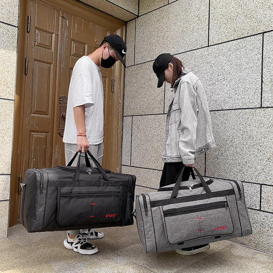 Two people with large gray duffel bags in front of a building.