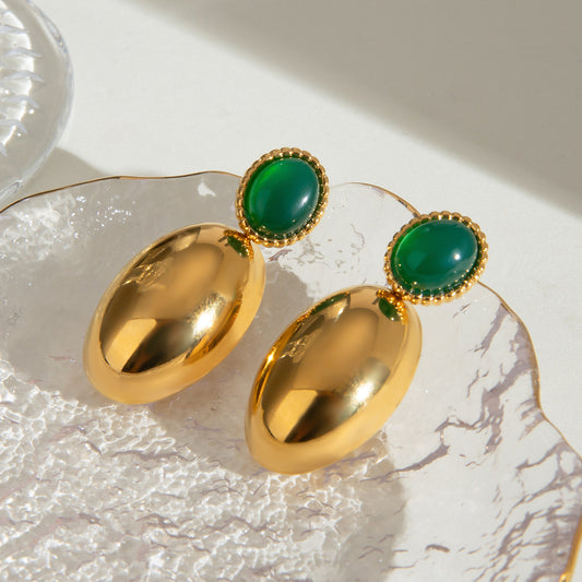 Gold earrings with green gemstones on a marble surface