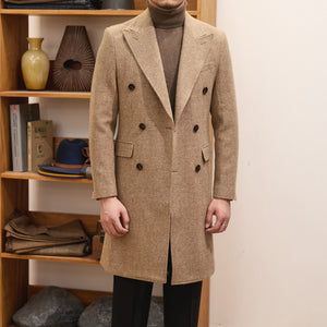 Person wearing a beige overcoat standing in front of a wooden shelf.