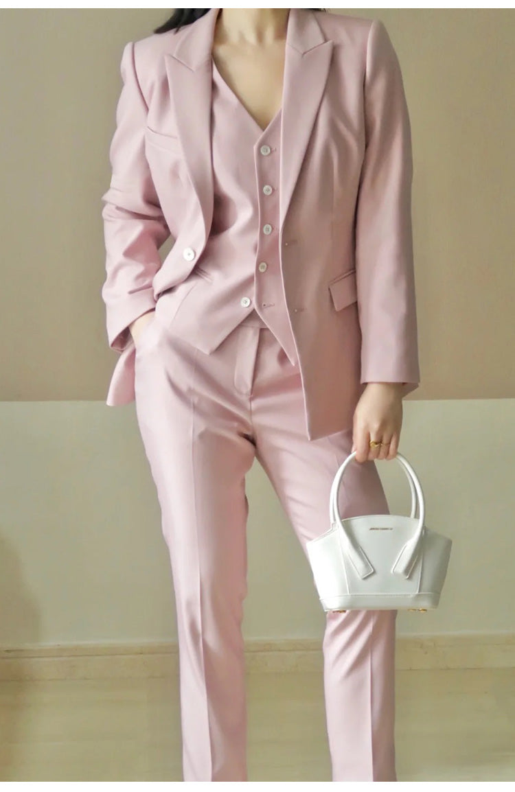 Person wearing a pink suit holding a white handbag against a plain background
