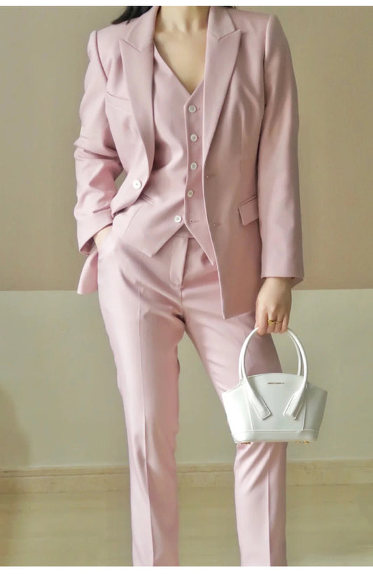 Person wearing a pink suit holding a white handbag against a plain background