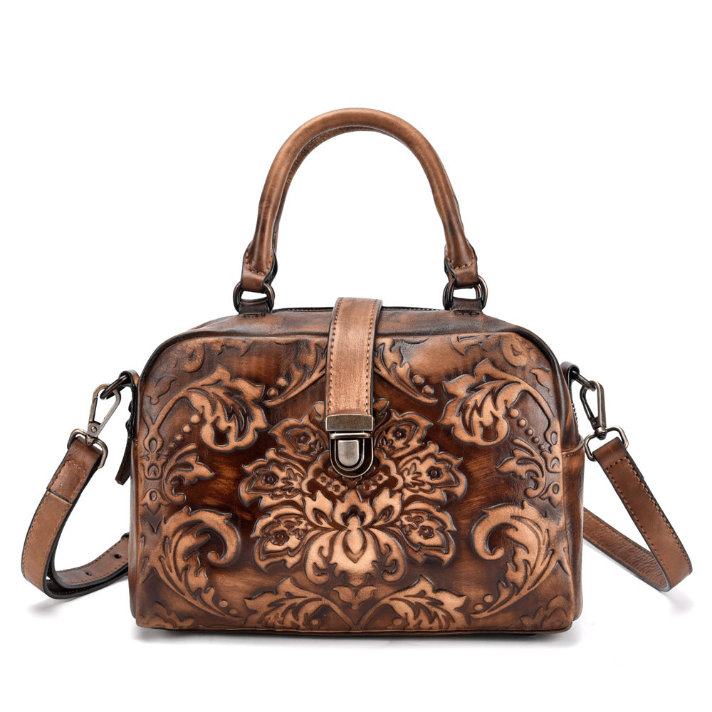 Brown leather handbag with intricate floral patterns on a white background