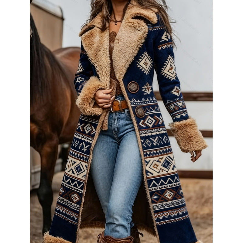 A woman wearing a long navy blue patterned coat with beige faux fur trim, blue jeans, and brown boots, standing in a barn-like setting with a horse partially visible in the background.