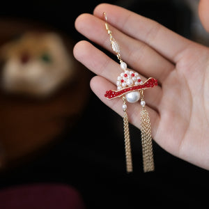 Decorative earring with red and gold design held by a hand against a blurred background
