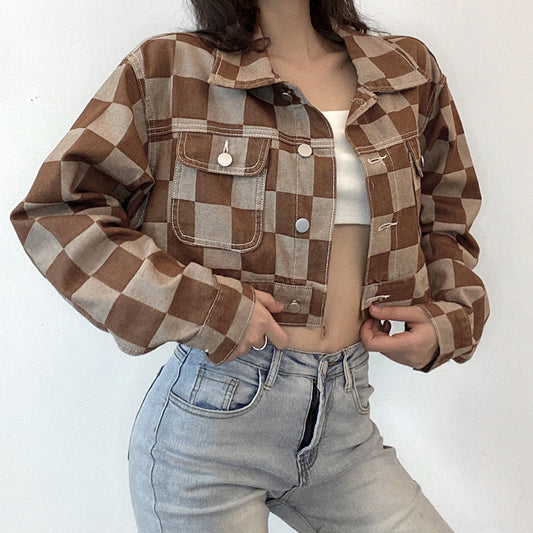 Person wearing a brown and beige checkered jacket with a white top and blue jeans on a white background