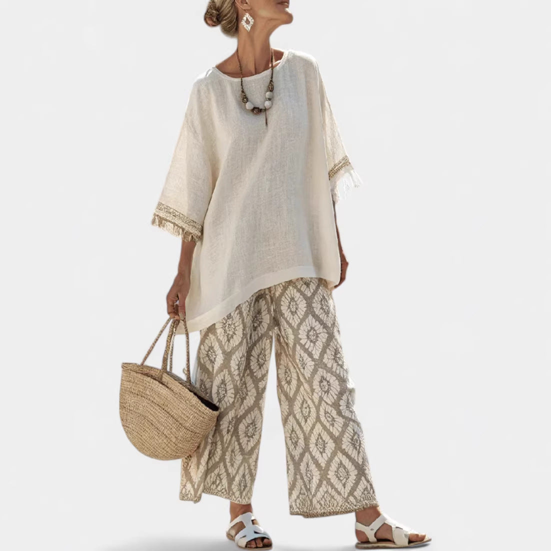 Woman wearing a beige top and patterned pants, holding a straw bag on a white background
