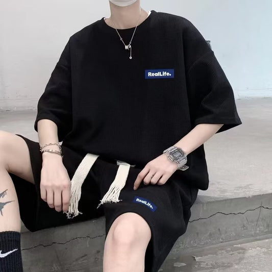 Person wearing a black oversized t-shirt with 'RealLife' logo sitting on the floor.