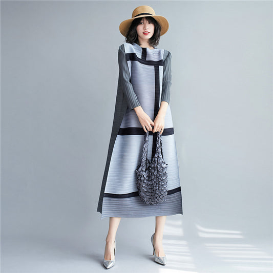 Woman wearing a stylish gray dress with black accents and a matching hat, holding a floral handbag on a plain background.