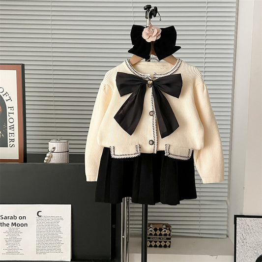 White sweater with a large black bow and black skirt on a mannequin against a neutral background.