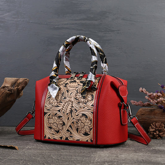 Red handbag with intricate leather design and patterned handle on a dark surface.